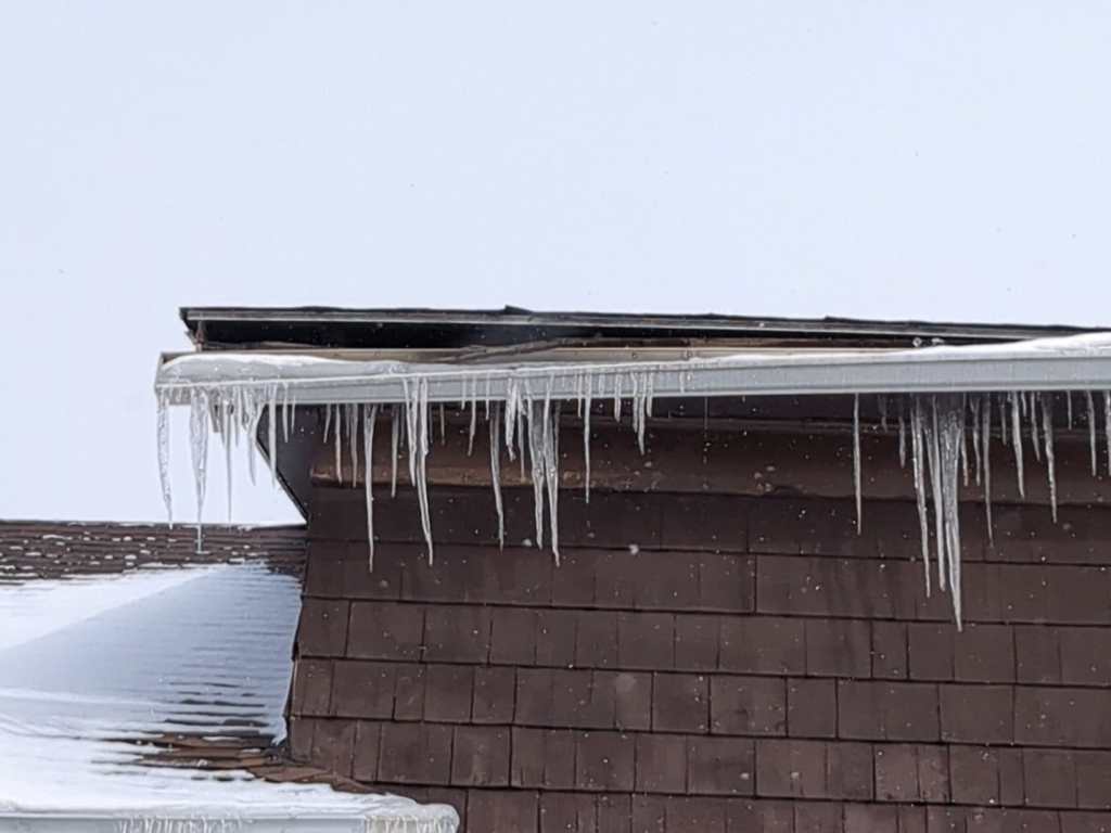 A damaged roof and gutter system in Erie County forming an ice dam and icicles.
